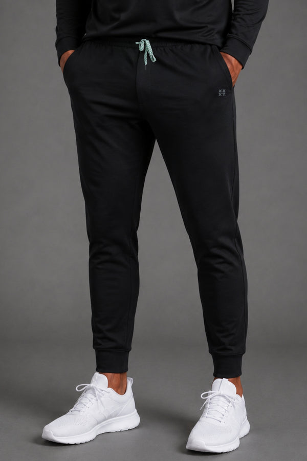 Front view of men’s black tapered joggers styled with a white T-shirt and white athletic sneakers. || Black