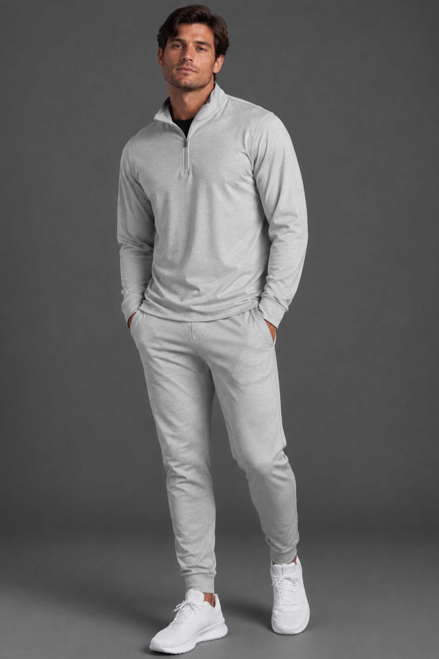 Male model wearing a light gray quarter-zip pullover with matching gray joggers and white sneakers against a dark gray studio background.|| Light Heather Gray - 1