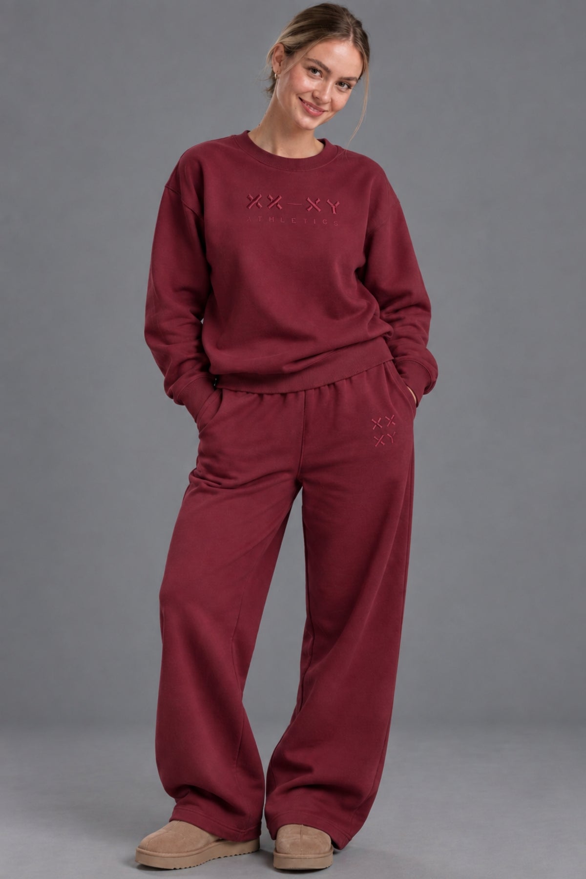 Woman wearing a burgundy XX-XY Athletics crewneck sweatshirt with matching wide-leg sweatpants.