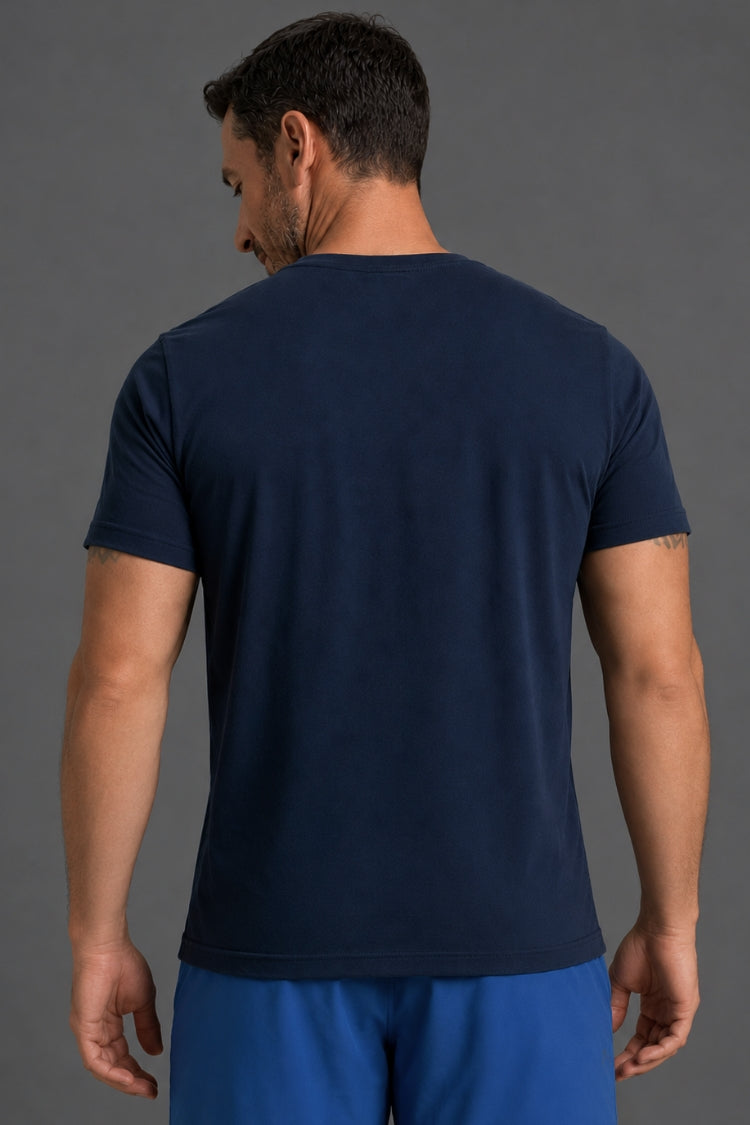 A man viewed from the back wearing a dark navy blue short-sleeve crewneck t-shirt and blue shorts against a solid gray studio background.
