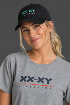Female model wearing XX-XY Athletics gray performance tee and black logo hat || Black