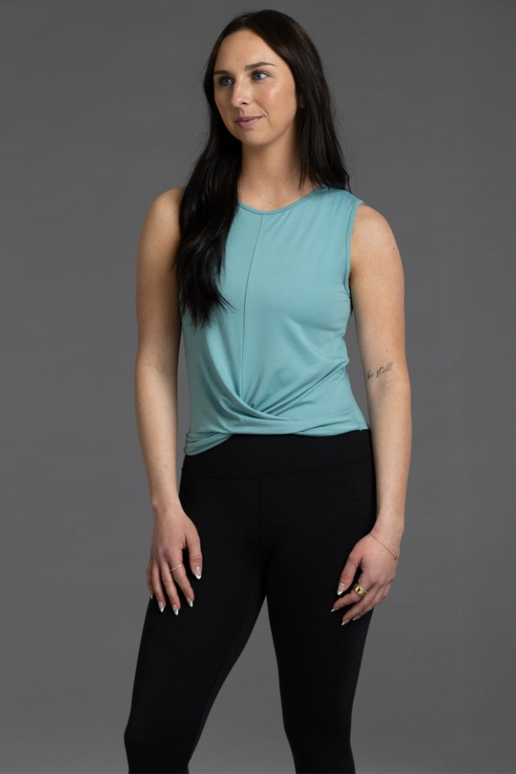 Woman wearing a teal sleeveless top and black pants against a gray background || Underseas