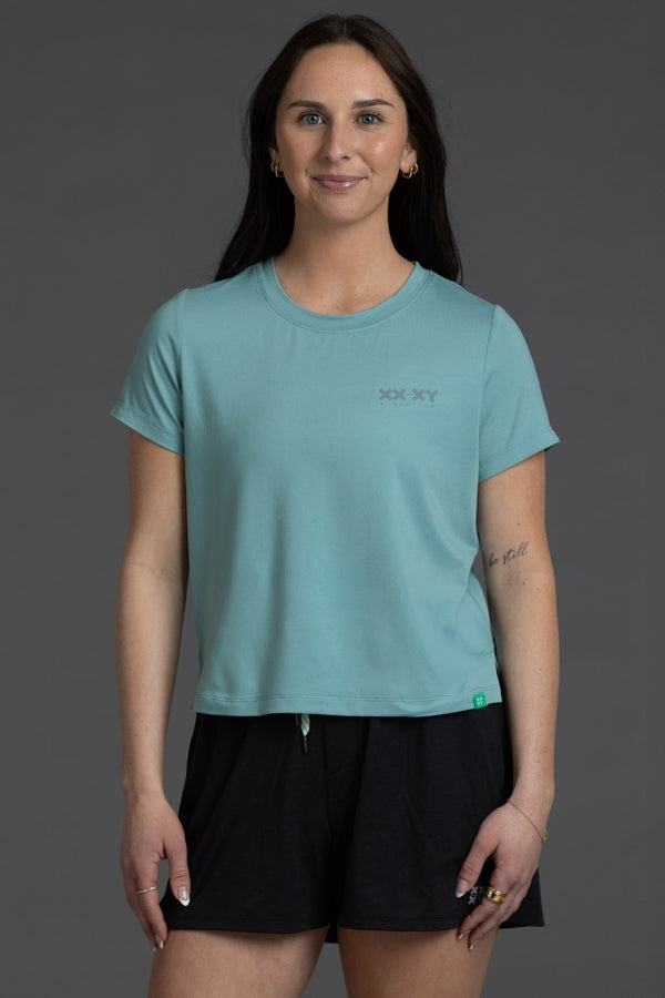 Woman wearing a light blue t-shirt with a logo on a gray background || Underseas