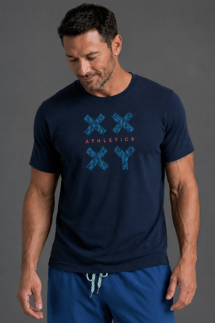 A man wearing a navy blue athletic t-shirt with a blue distressed 'XX' and 'ATHLETICS' graphic on the chest, paired with blue athletic shorts, against a dark gray studio background. || Navy Camo