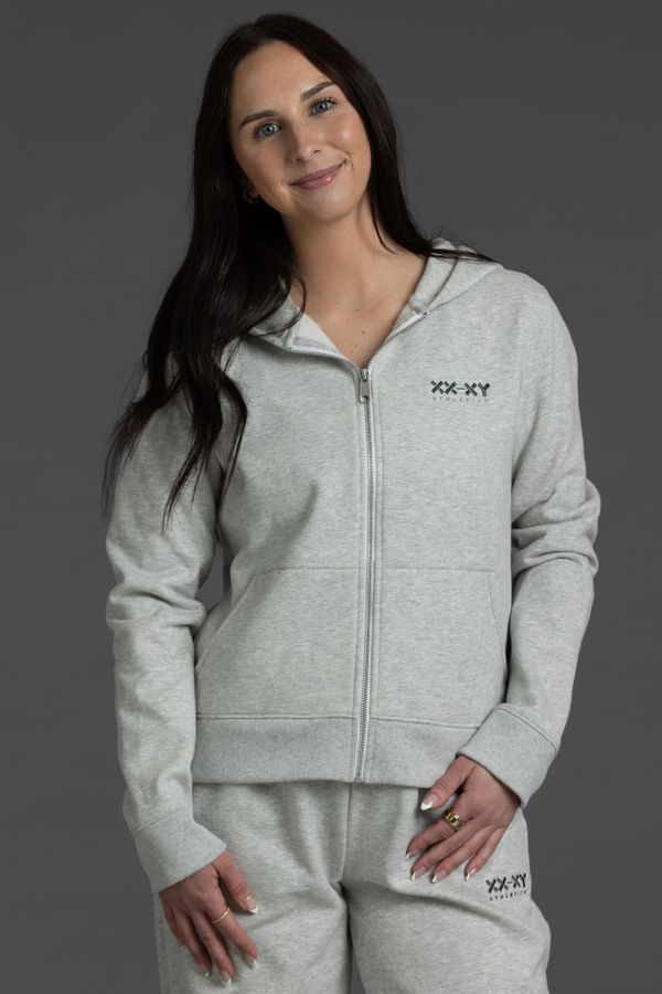 Woman wearing a gray tracksuit with a brand logo on a gray background || Light Heather Gray