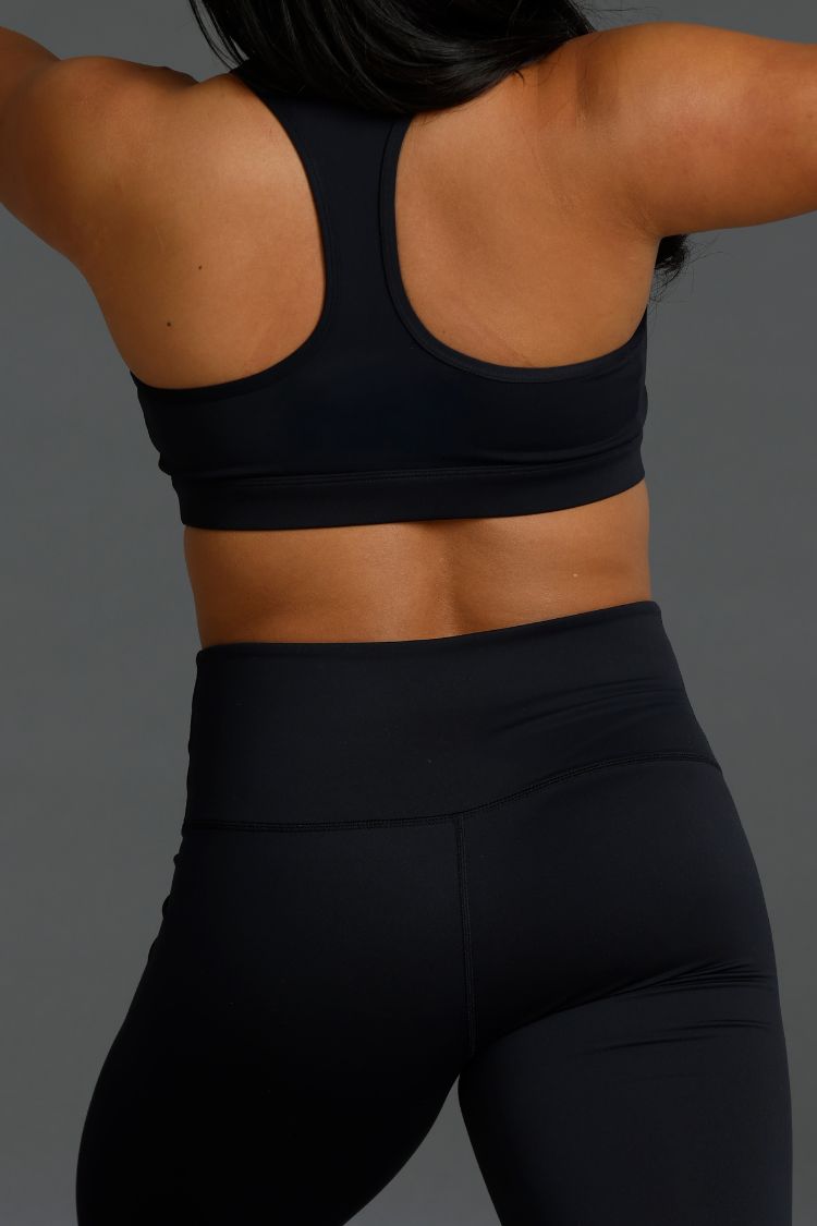 Person wearing a black sports bra and leggings on a gray background || Black
