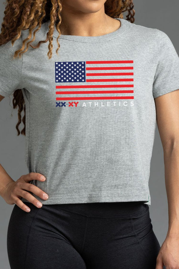 Person wearing a gray t-shirt with an American flag and 'XY Athletics' logo. || Light Heather Gray