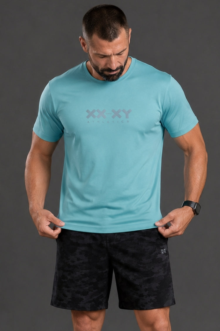 Man wearing a turquoise t-shirt with a logo and black shorts on a gray background || Underseas