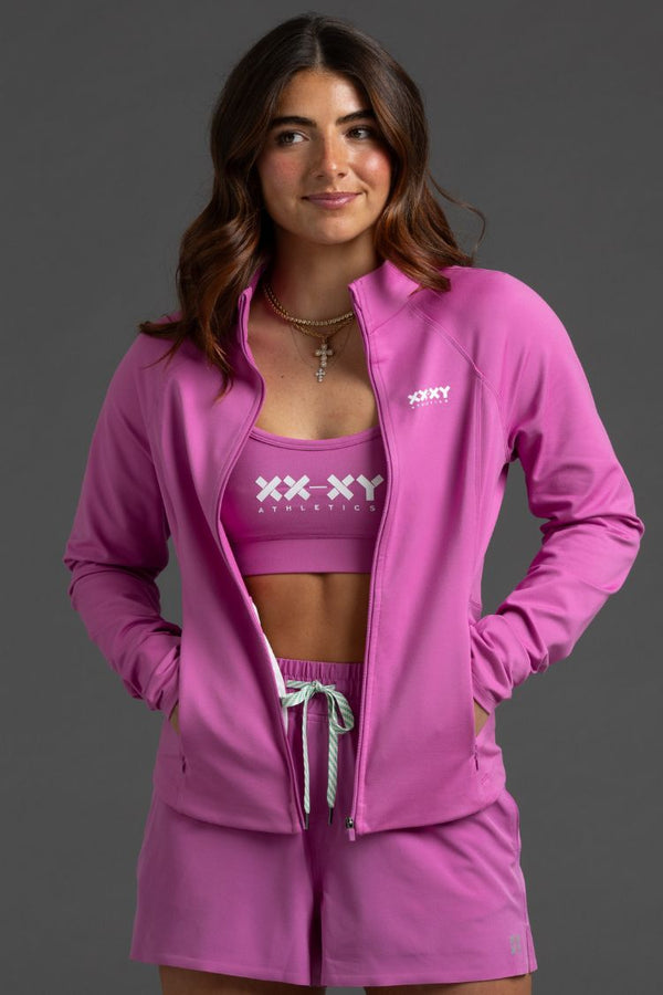 Woman wearing a pink athletic outfit with 'XXXY' branding on a gray background || Bright Fuchsia