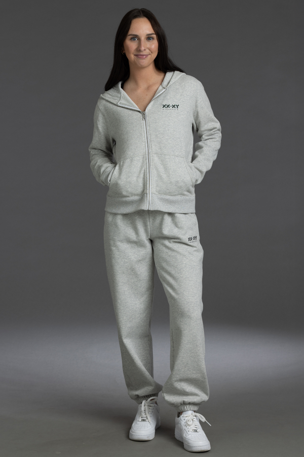 Woman wearing a gray tracksuit with a brand logo on a gray background || Light Heather Gray