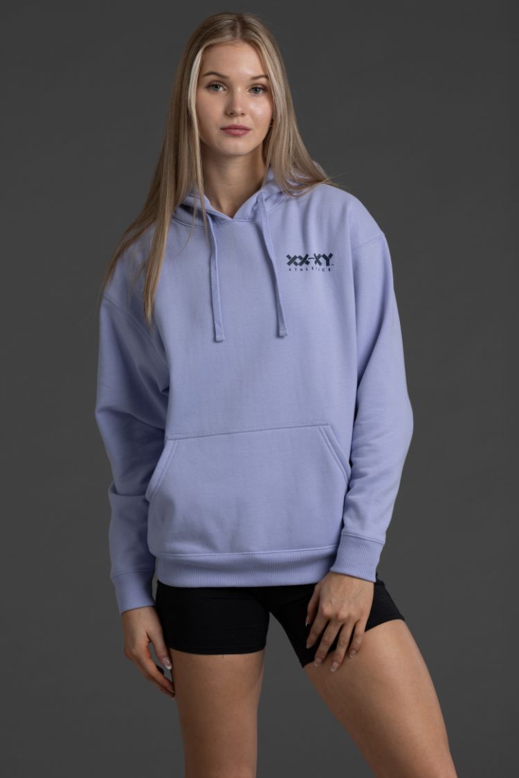 Woman wearing a light blue hoodie with a logo on a dark gray background || Lavender Gray