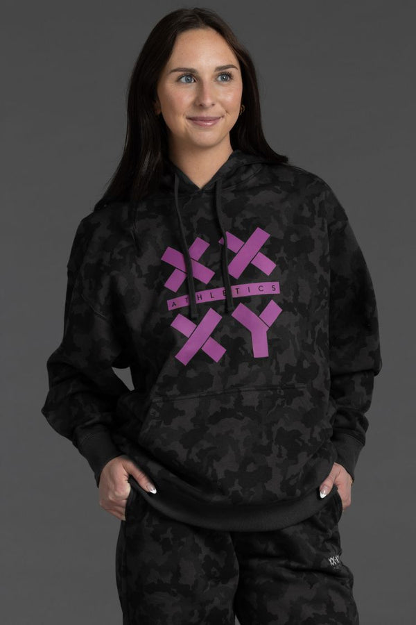 Person wearing a black camouflage hoodie with purple logo on a gray background || Black Camo