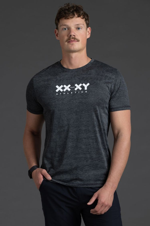 Man wearing a dark gray t-shirt with a logo on a gray background || Black