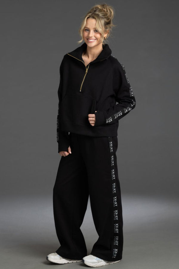 Woman wearing a black tracksuit with sequin details on a gray background || BLACK