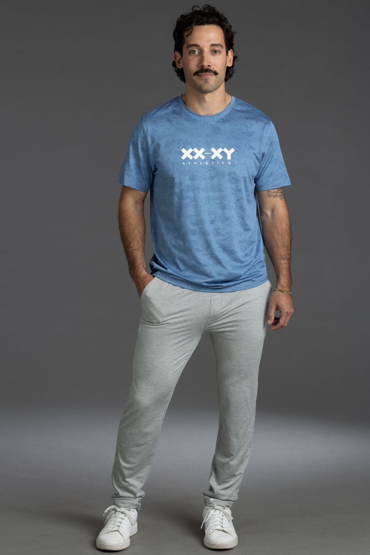 Man wearing a blue t-shirt with white text and light gray pants on a gray background || Light Heather Gray - 1