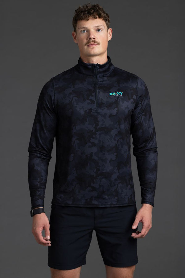 Man wearing a dark patterned long-sleeve shirt and black shorts on a gray background || Black Camo