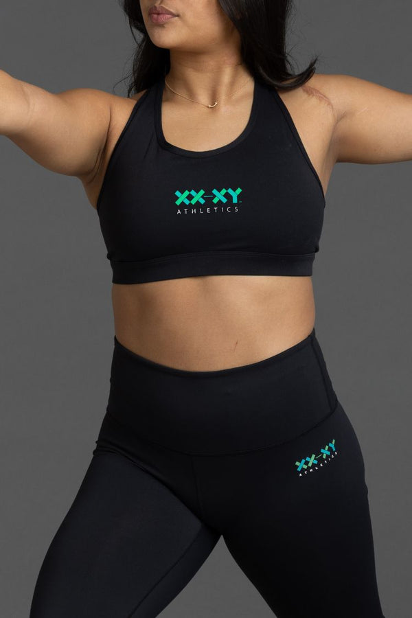 Person wearing black athletic bra and leggings with 'XXXY Athletics' logo || Black