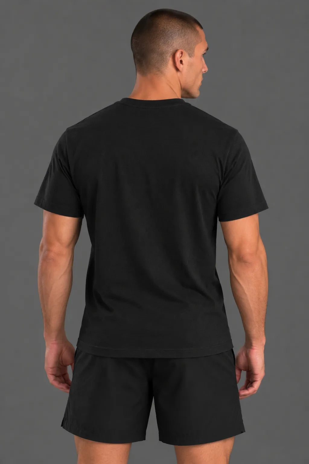 Male model showcasing the plain black back of an XX-XY Athletics crewneck T-shirt, paired with black athletic shorts against a gray studio background. || Black