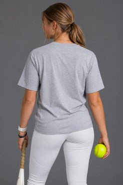 Back view of female softball player wearing a blank gray V-neck T-shirt and white softball pants while holding a bat and softball. || Light Heather Gray