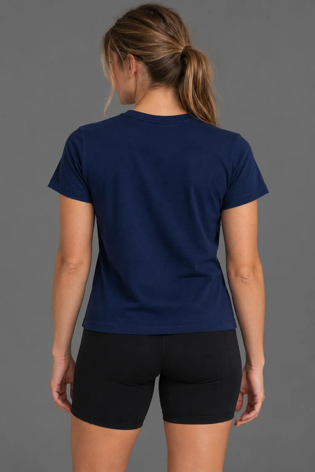 Back view of a female model wearing a blank navy tee with black bike shorts. || Navy