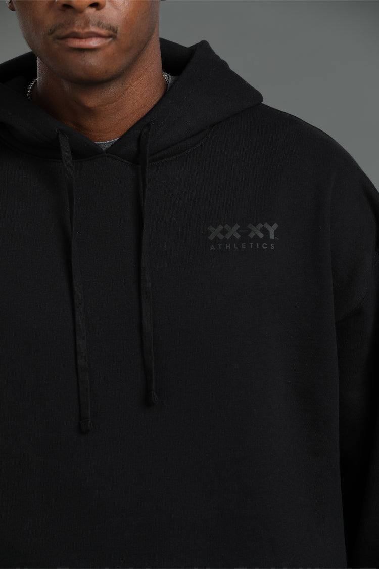 Person wearing a black hoodie with a logo on the chest against a gray background || Black