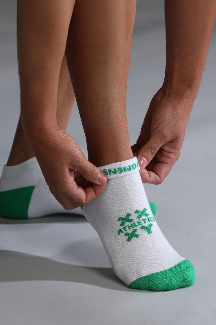 Person wearing a white sock with green accents and text on a neutral background || white