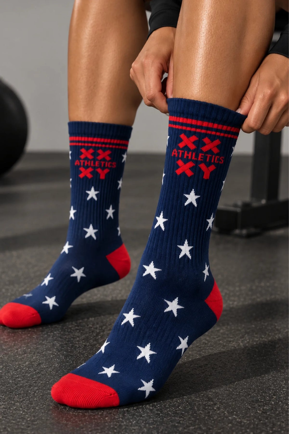 Woman pulling on navy XX-XY Athletics crew socks with white stars and red accents in a gym.