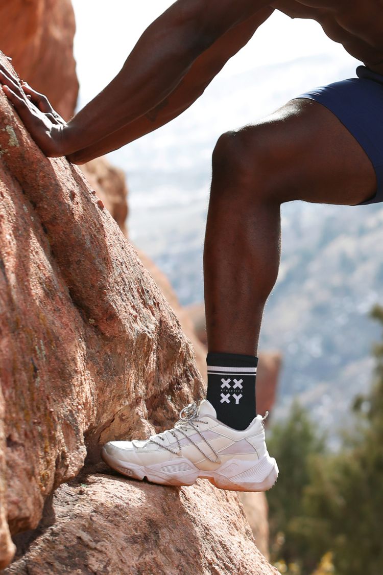 Person climbing a rock face wearing white sneakers and a black sock with a brand logo. || black
