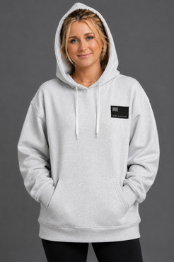 Woman wearing a gray hoodie with a small black logo on a gray background || Light Heather Gray