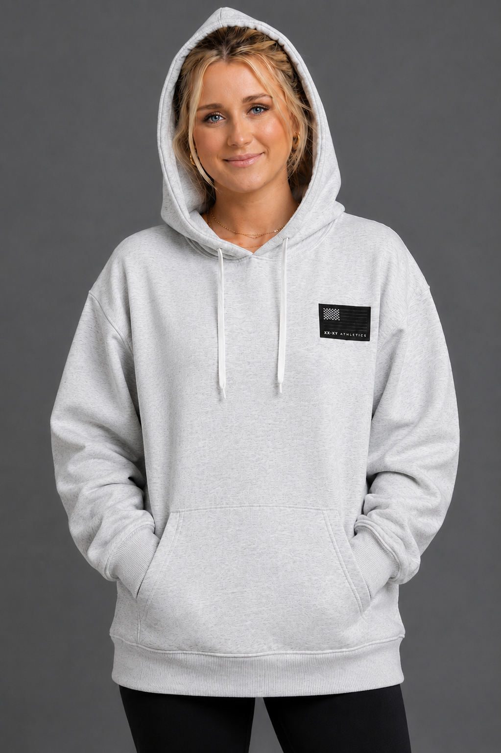 Woman wearing a gray hoodie with a small black logo on a gray background || Light Heather Gray