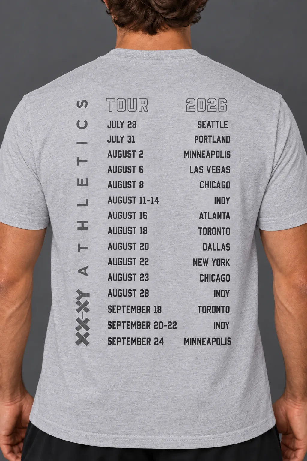 A man wearing a white t-shirt, viewed from the back. The shirt features a black printed schedule of '2026 Tour' dates for 'Athletics' on the back. || Light Heather Gray