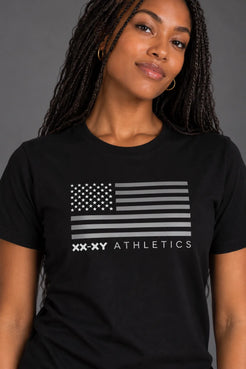 Close-up of female model wearing a black XX-XY Athletics tee featuring a gray American flag graphic and logo || Black