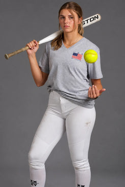 Female softball player wearing a gray USA XX-XY Athletics V-neck T-shirt, holding a softball and bat. || Light Heather Gray