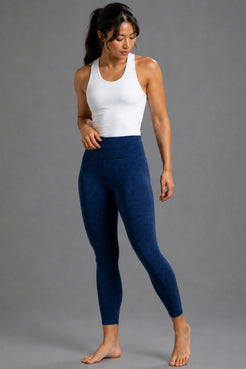 A woman modeling high-waisted navy blue leggings and a white tank top against a solid gray studio background.  || White