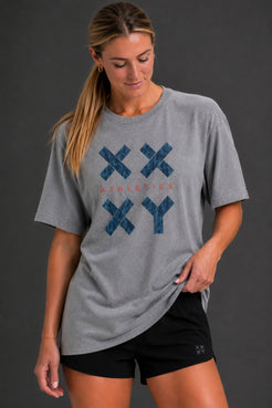 A woman wearing a heather gray athletic t-shirt with a blue distressed 'XXYY' graphic and black athletic shorts, posed against a dark gray studio background. || Heather Gray
