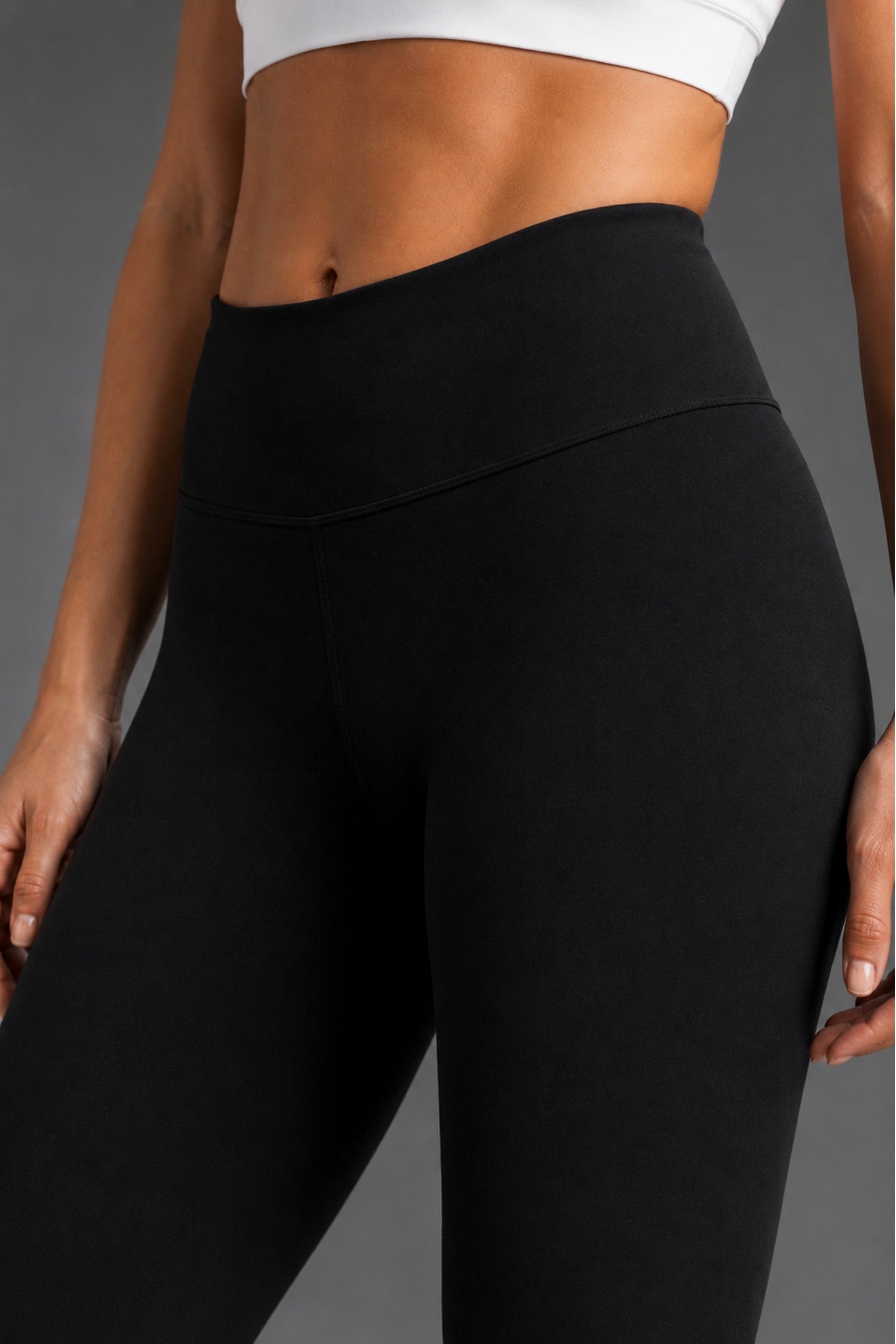 Close-up of a model wearing black high-waisted athletic leggings with a white sports bra against a neutral gray background. || Black Heather