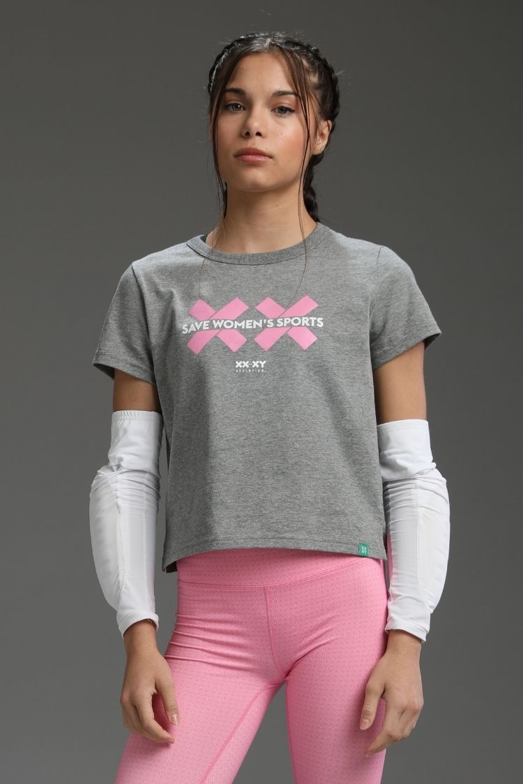 Woman wearing a gray t-shirt with pink graphics and text, standing against a gray background
