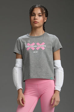 Woman wearing a gray t-shirt with pink graphics and text, standing against a gray background || Heather Gray
