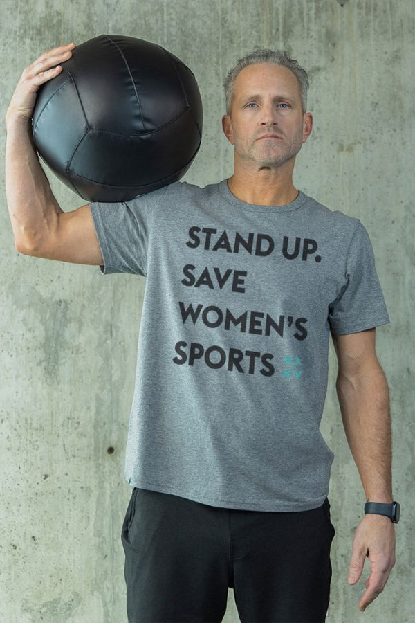 Man holding a medicine ball wearing a gray t-shirt with text against a concrete wall. || heather gray