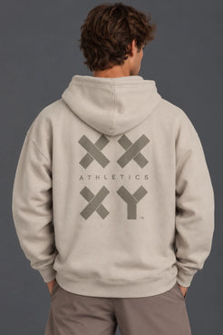 Back view of a male model wearing a beige XX-XY Athletics graphic hoodie with mocha shorts. || Taupe