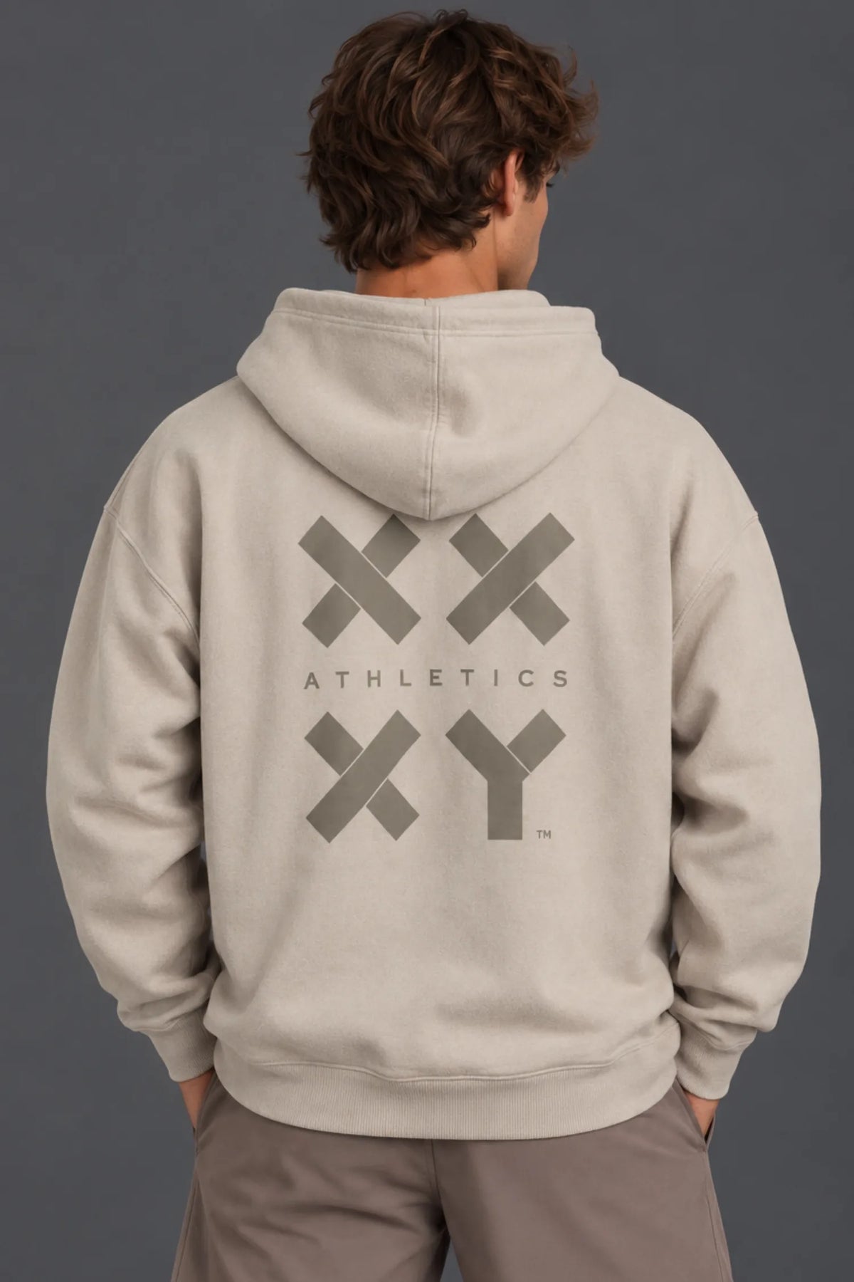 Back view of a male model wearing a beige XX-XY Athletics graphic hoodie with mocha shorts. || Taupe
