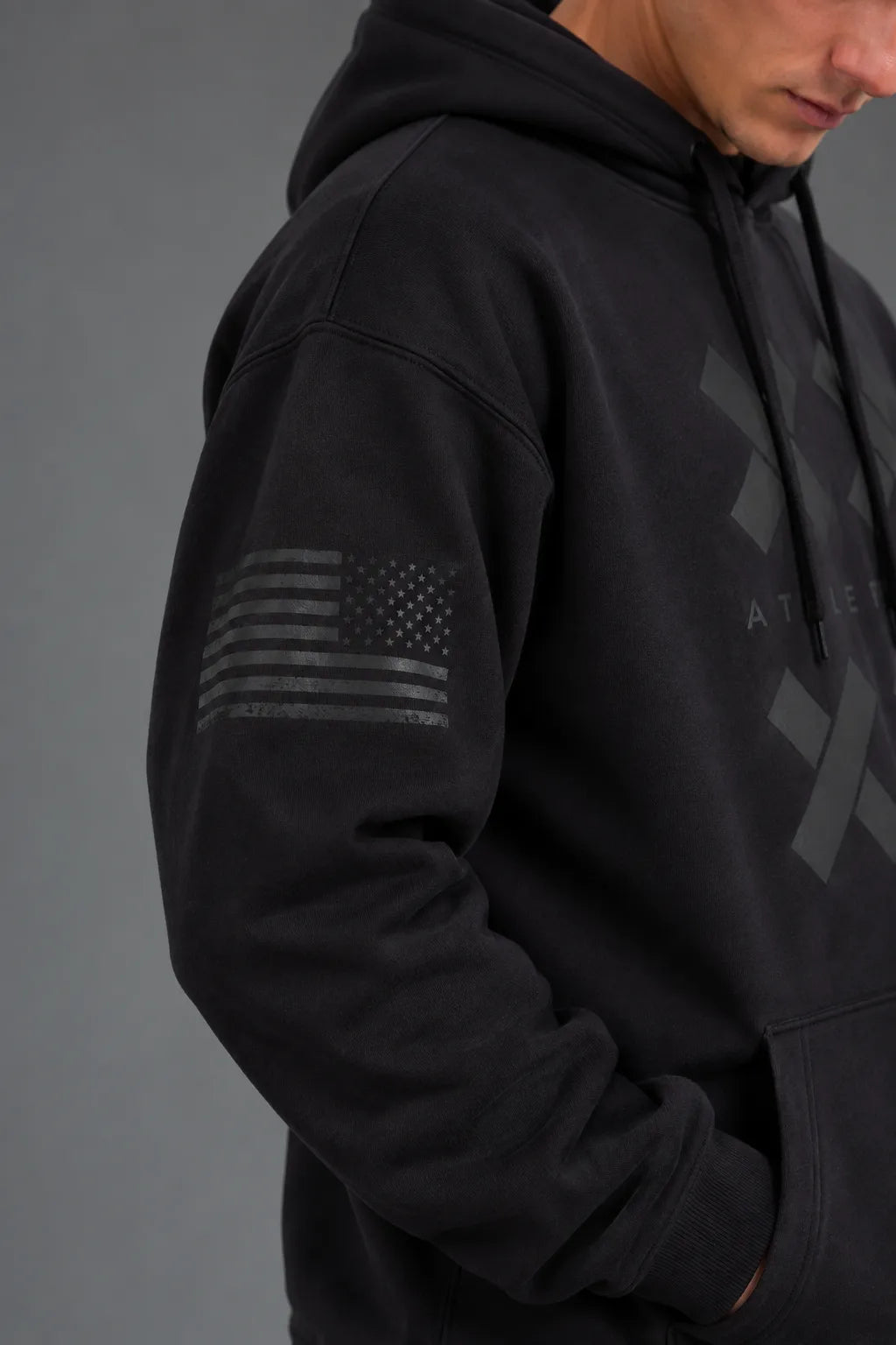Close-up of the tonal American flag graphic on the sleeve of a black XX-XY Athletics hoodie. || Black
