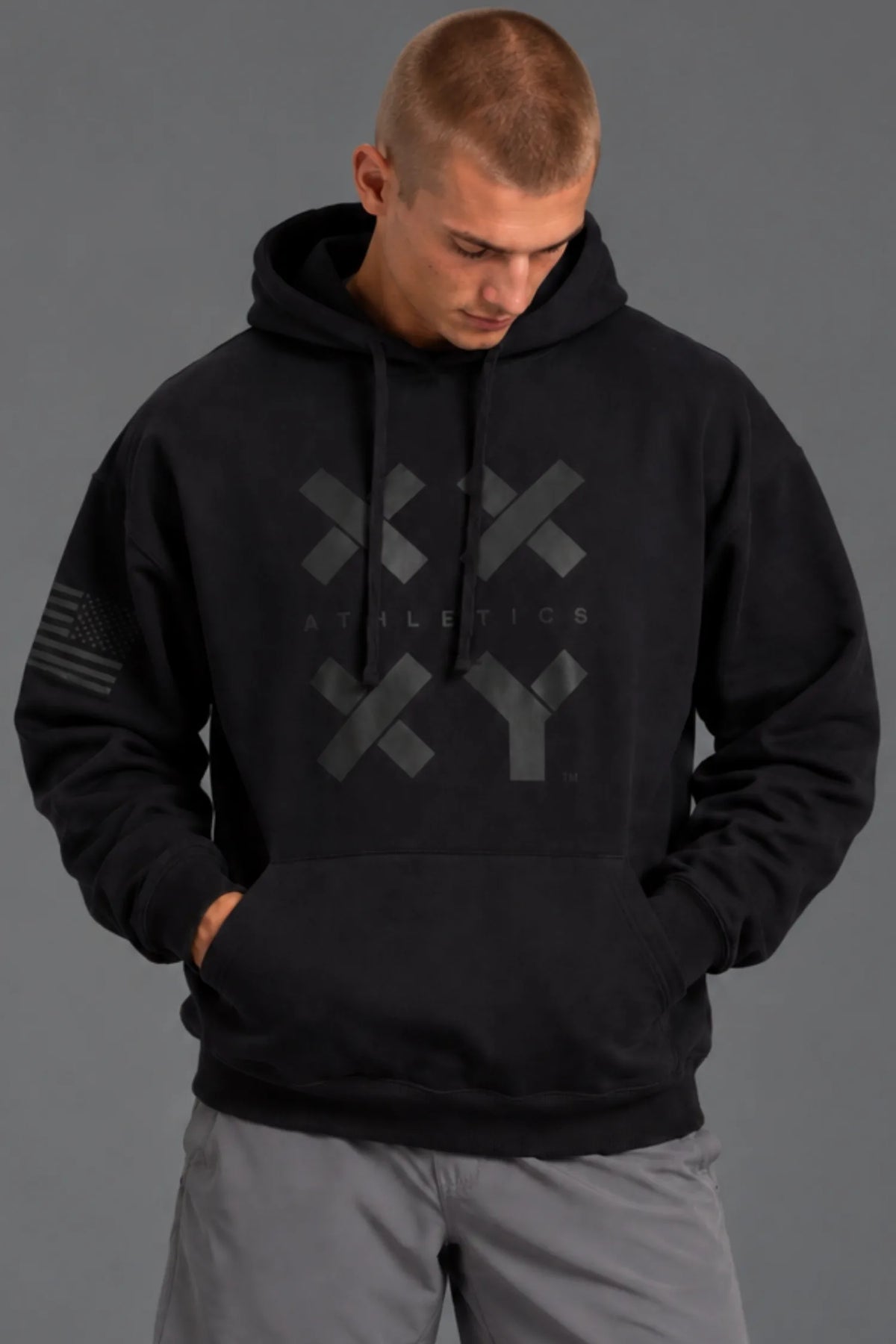 Male model looking down while wearing a black XX-XY Athletics hoodie with gray shorts. || Black