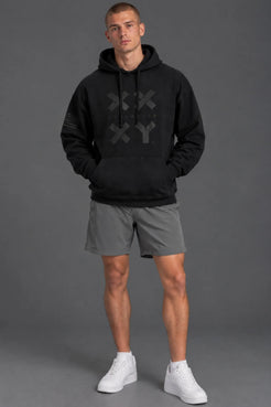 Male model wearing a black XX-XY Athletics graphic hoodie with gray athletic shorts against a gray studio background. || Black
