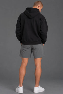 Back view of a male model wearing a blank black hoodie with gray athletic shorts. || Black