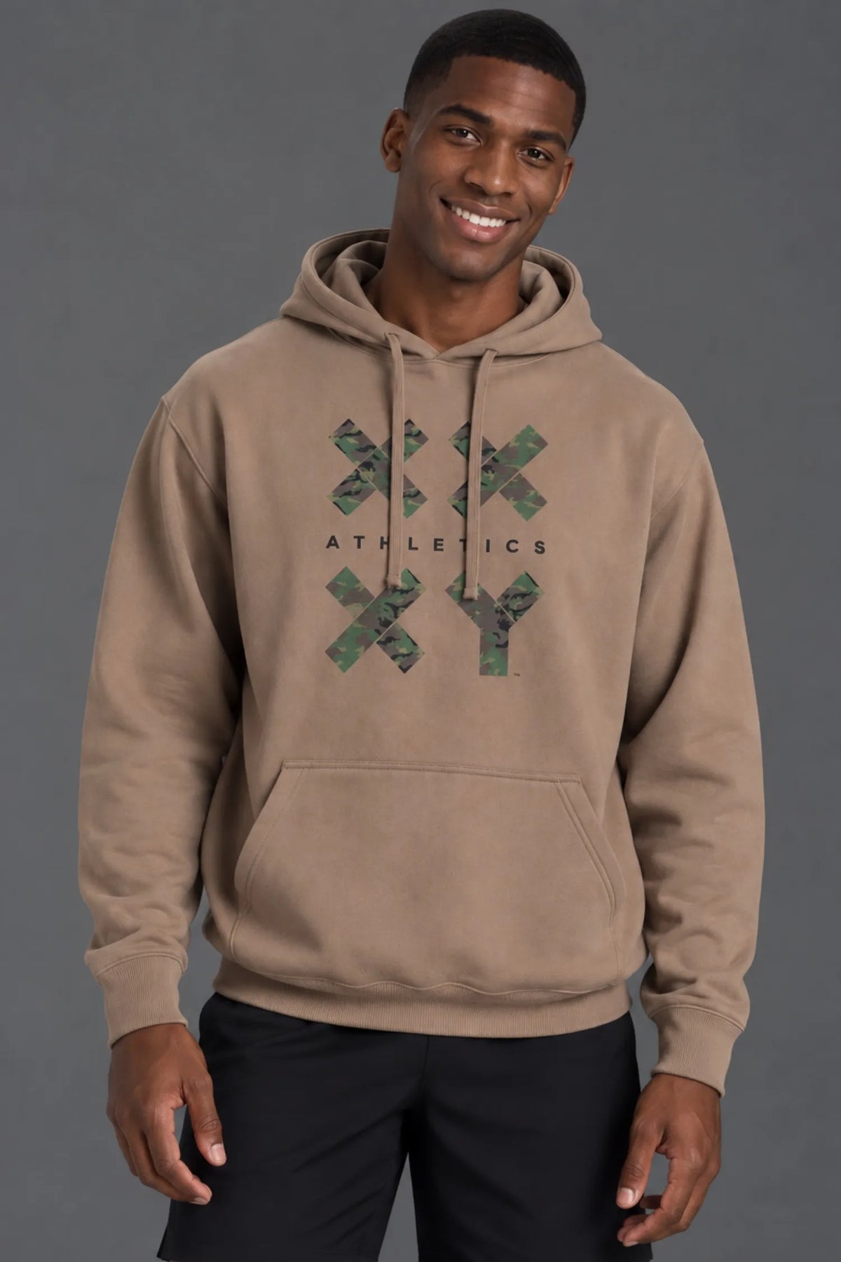 Male model smiling while wearing a mocha XX-XY Athletics camo graphic hoodie with black shorts. || Mocha
