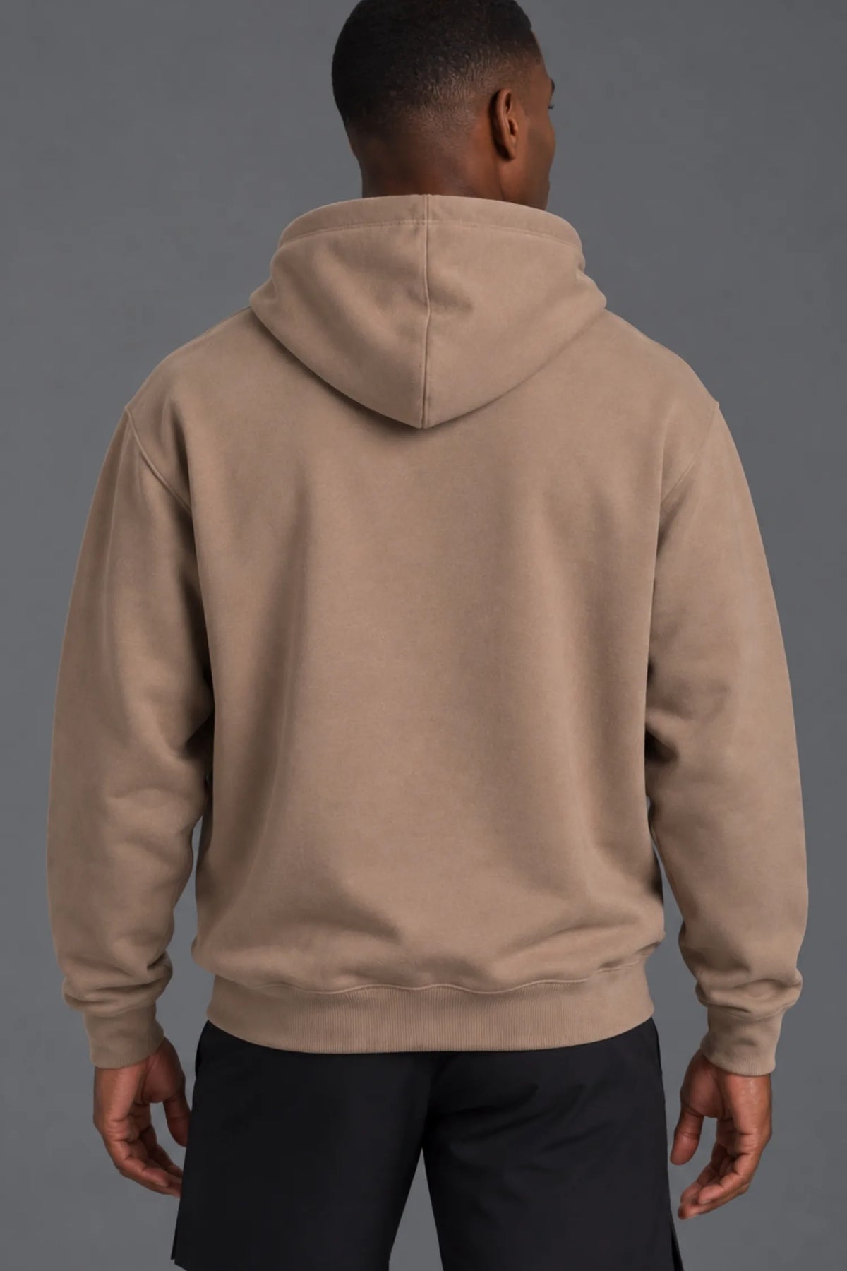 Back view of a male model wearing a blank mocha hoodie with black athletic shorts against a gray background.