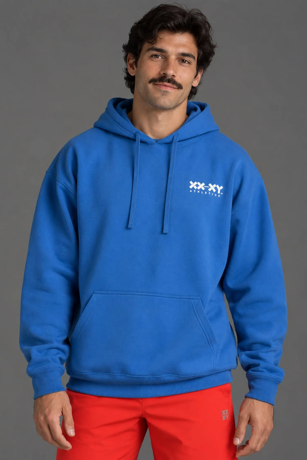 Male model wearing a blue XX-XY Athletics hoodie and red shorts, highlighting the hoodie’s fit and chest logo. || Cobalt Blue
