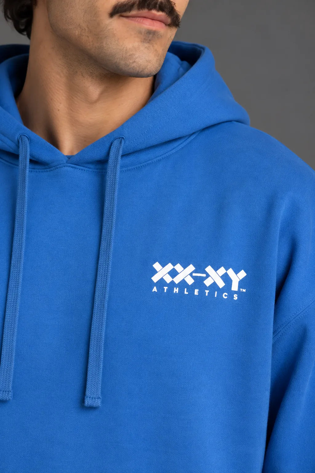 Close-up of the white XX-XY Athletics logo and fabric texture on a blue hoodie. || Cobalt Blue