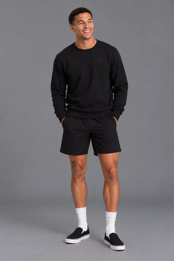 Male model laughing while wearing the XX-XY Athletics Crewneck Sweatshirt, black shorts, white crew socks, and black slip-on sneakers || Black